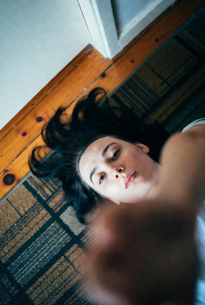 A low-angle, slightly tilted shot of a young woman lying on the carpet, hair fanned out, looking up tiredly — intimate and exhausted vibe. A low-angle, slightly tilted shot of a young woman lying on the carpet, hair fanned out, looking up tiredly — intimate and exhausted vibe.