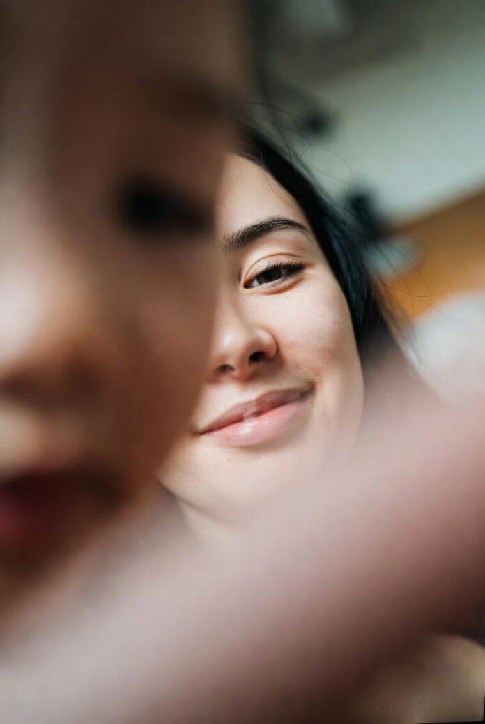 Low-angle toddler's view: mom's tired smile half in shadow, chaos softly blurred behind her. Low-angle toddler's view: mom's tired smile half in shadow, chaos softly blurred behind her.