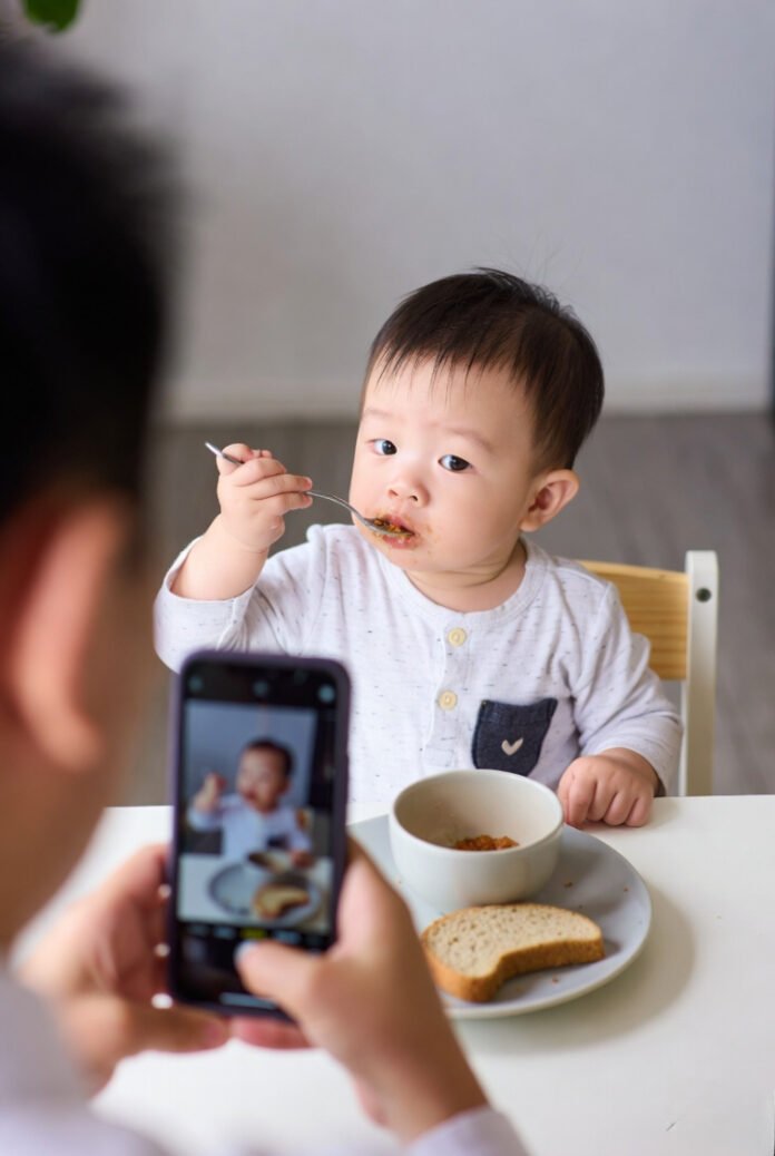 Messy-faced baby eating, phone screen showing the same scene. Messy-faced baby eating, phone screen showing the same scene.