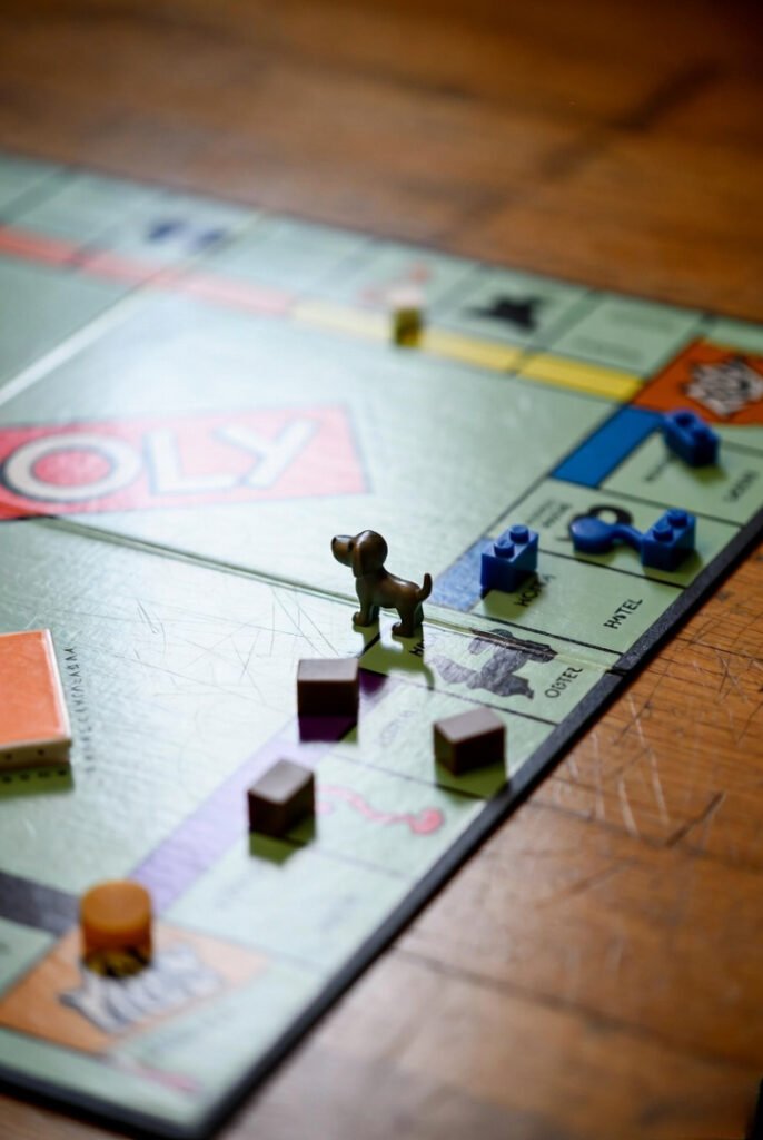 Close-up of a battered Monopoly board on scratched hardwood: hotels toppling, missing dog token swapped for a blue Lego piece.