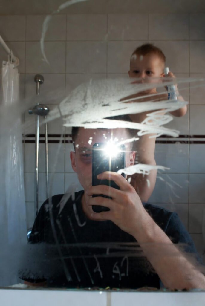 "Day 15 mirror selfie: dark circles, harsh flash, toddler drawing on steamed mirror with toothpaste"