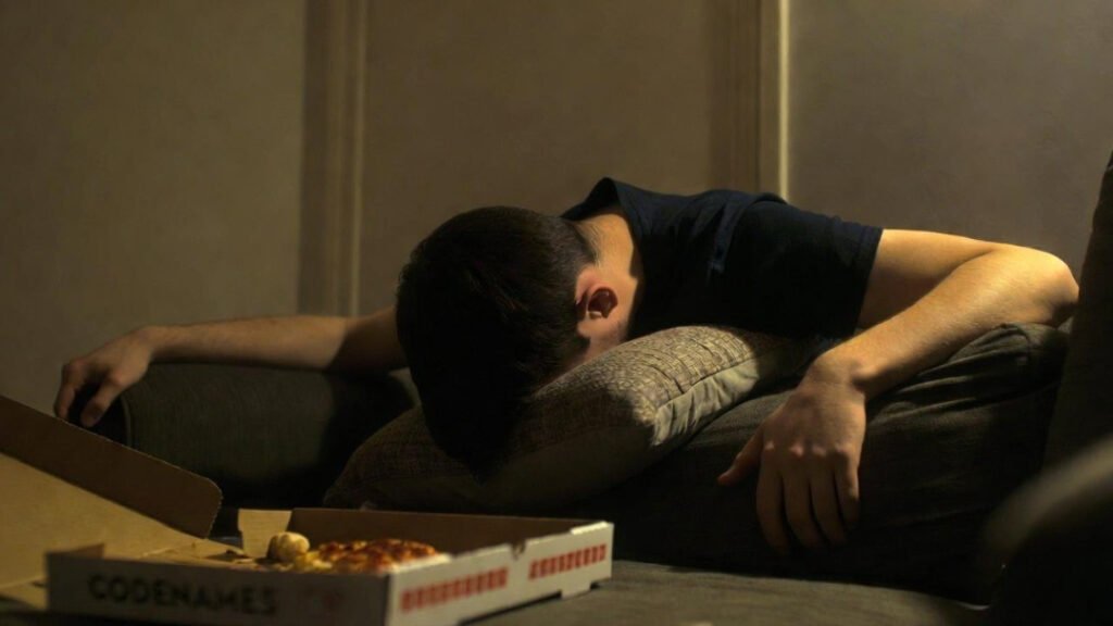 teen dramatically face-planted into pillow after Codenames meltdown, pizza remnants nearby.